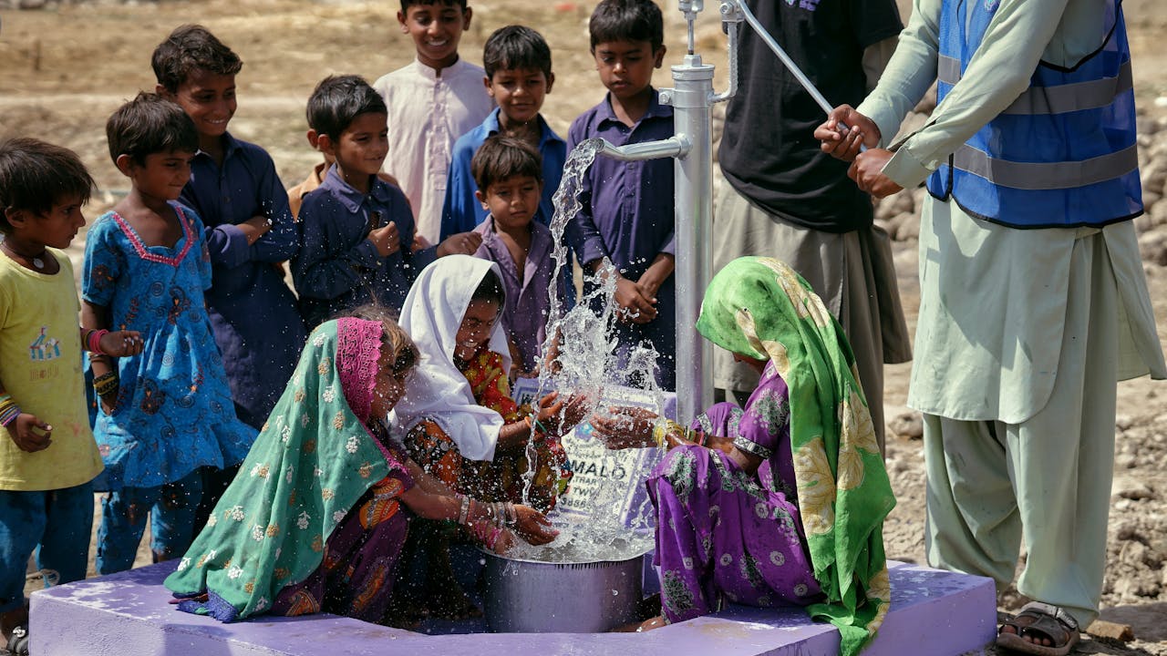 Group of children collecting clean water from a pump in an outdoor setting.